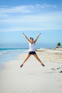 Joyful woman celebrating running and sport success. Female athlete jumping at tropical beach. Sport goals concept.