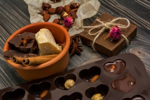 Homemade chocolate candys, cocoa, cocoa butter, nuts, present box, cinnamon and dry roses on wooden background