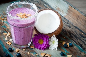 Healthy mixed berry smoothie milkshake made from blended blueberries, strawberries  with yogurt. Served in a coconut frosted glass with half coconut shell.